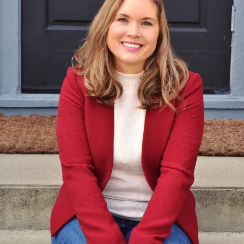 Woman wearing a red shirt and jeans sitting on cement stairs
