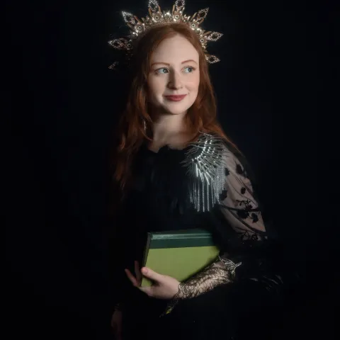 Kaitrin standing against a black background with a crown and a green book.