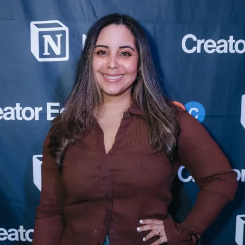 Mimi gonzalez, a brown skinned woman with straight hair dressed in brown long sleeve shirt against a blue background