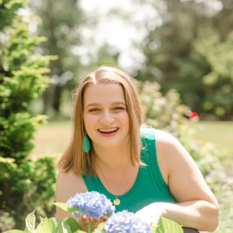 Picture of Lauren Simpson smiling in a garden while wearing a green tank top and green drop earrings.