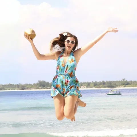 Deanna Troy Travels jumping on a beach in Indonesia with a coconut.