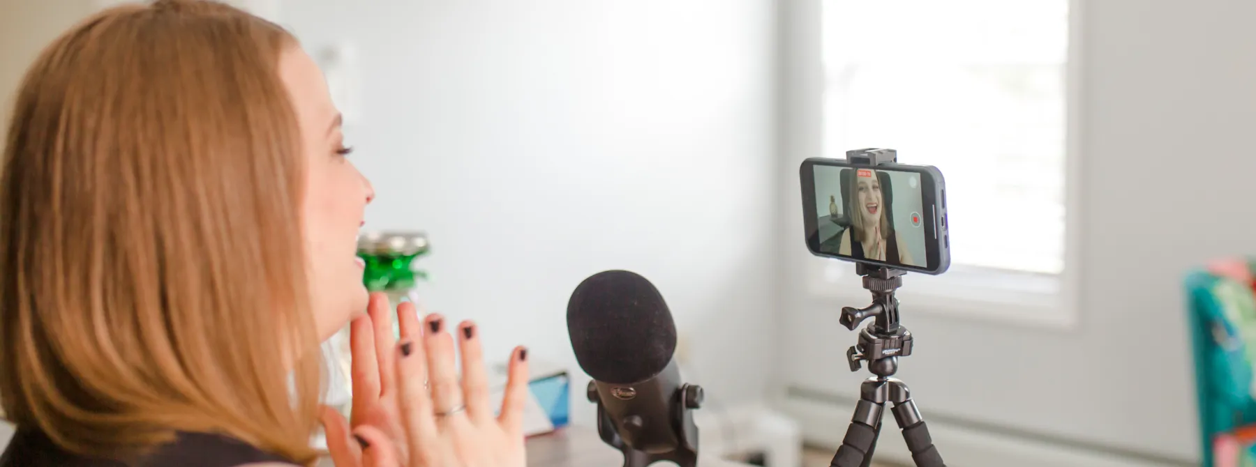 Lauren Simpson filming a video on the front facing camera of her iPhone with a Yeti microphone sitting on the desk next to it.