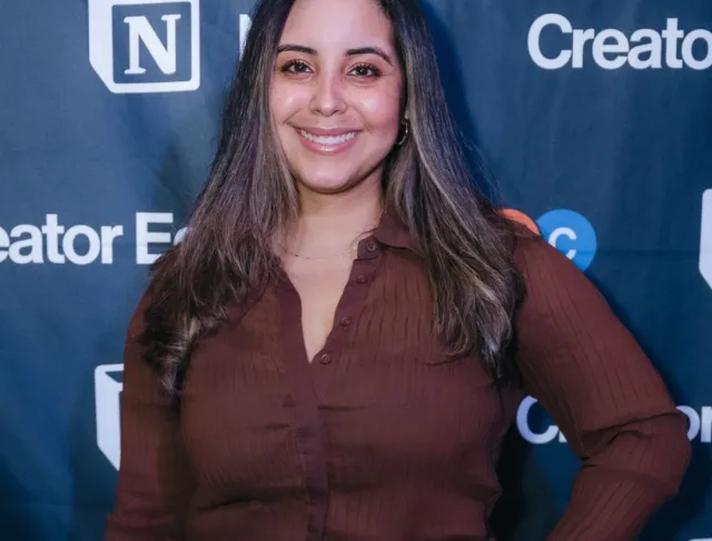 Mimi gonzalez, a brown skinned woman with straight hair dressed in brown long sleeve shirt against a blue background