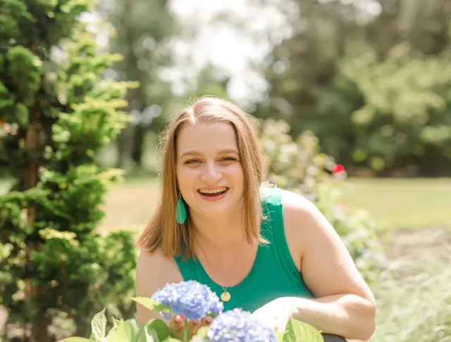 Picture of Lauren Simpson smiling in a garden while wearing a green tank top and green drop earrings.